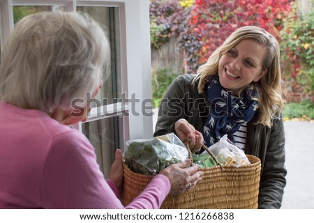 Female Neighbor Helping Senior Woman With Shopping Royalty-Free Stock Photo #1216266838