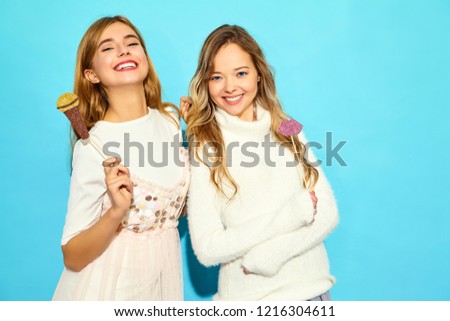 Two young beautiful woman singing with props fake microphone.Trendy girls in casual summer clothes. Positive female emotion with big lips on stick. Funny models isolated on blue background