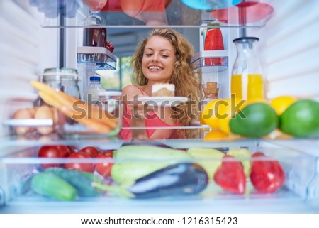 Woman taking gateau form fridge full of groceries. Unhealthy eating concept. Picture taken from the inside of fridge.