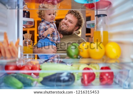 Father and son standing in front of opened fridge and looking something to eat at night. Fridge full of groceries. Picture taken from the iside of fridge.