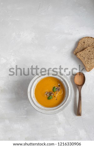 Minimal picture - pumpkin soup plate with bread and wooden spoon. Top view, gray background, copy space.