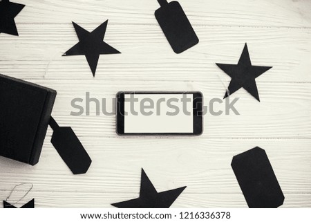 Phone with empty screen black gift box and price tags on white background. Space for text. Black Friday Sale flat lay. Christmas shopping and sales. Advertising app. Cyber monday