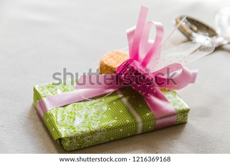 A small gift wrapped with a green wrapping paper with a pink ribbon placed over a table with a white tablecloth 