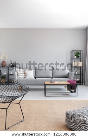 Vertical view of elegant grey living room with comfortable couch, metal shelves and wooden coffee table, real photo with copy space