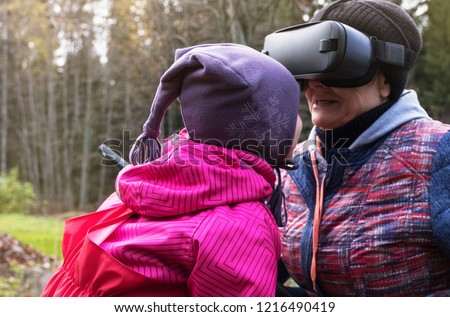 An elderly woman and a little girl are having fun playing in the Park. On an elderly lady wearing virtual reality glasses