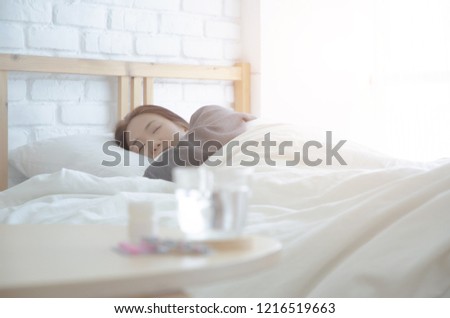 Asian woman wearing uncomfortable shirts are taking medication with pink tablets.In the white bedroom There are girl on the bed. And she was sick.