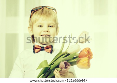 Happy smiling cute little boy gentleman with blonde hair in white shirt and bow tie holding beautiful fresh spring bouquet of colorful tulips for mothers day holiday, horizontal picture