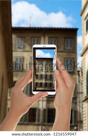 A tourist is taking a photo of part of the facade of an old residential building in the historic part of Florence, Italy on a mobile phone