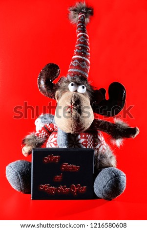 Congratulations on the new year. On a red background sits a toy moose and holds a sign with congratulations