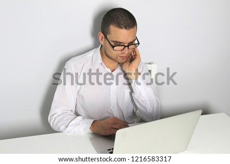 Handsome young man. Male in glasses. White table. White background. Emotional face with expression. Laptop computer on table.