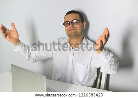 Handsome young man. Male in glasses. White table. White background. Emotional face with expression. Laptop computer on table.