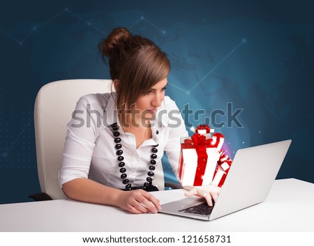 Pretty young lady sitting at desk and typing on laptop with present boxes icons