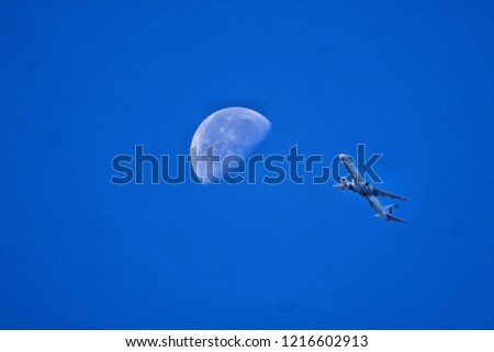 Daytime Moon with dark blue skies and airplane flying closeby in photo