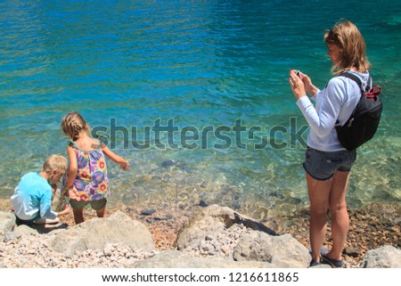 mummy takes pictures of her children playing on the shore of karst lake in the mountains