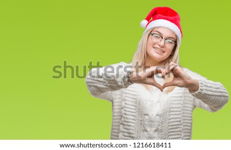 Young caucasian woman wearing christmas hat over isolated background smiling in love showing heart symbol and shape with hands. Romantic concept.