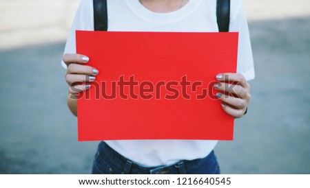 Blank red paper in hands of young woman with fingernails painted on blue background for text or copy space 