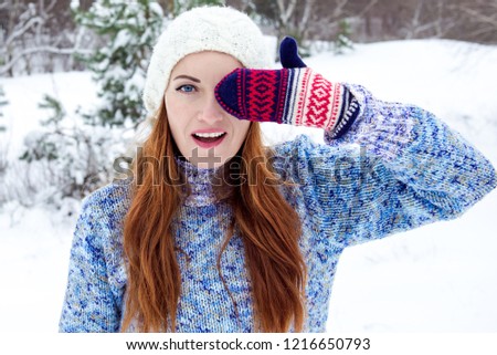 Portrait of a winter woman. Portrait of a smiling girl on a winter background. One gloved hand covers half the face