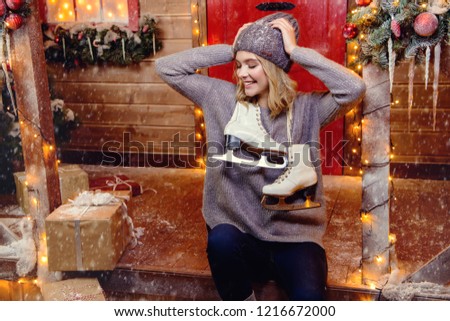 Happy girl in a warm winter clothes and skates in her hands, stands near the house decorated for Christmas. Time for miracles. Merry Christmas and Happy New Year.