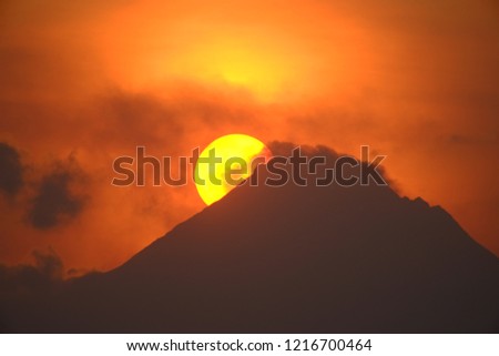 Sunrise behind Mount Merapi at Central Java, Indonesia. Sunrise on the moutain. Dramatic morning sky. The sun looks round behind a mountain and covered in a thin cloud
