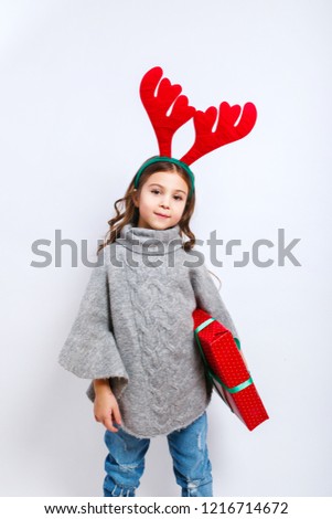 Happy little smiling girl with christmas gift box looking in camera. Christmas concept. Smiling funny girl in deer horns in studio.