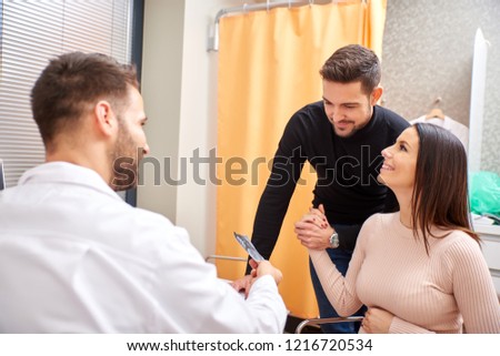 A handsome male doctor shows ultrasound picture to the young pregnant couple.