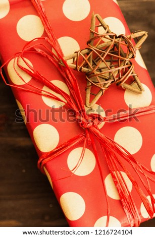 Christmas and New Year's Day festive decoration, wooden star with present wrapped in red paper with golden circles on brown wood background. Flat lay. View from above. Copy space for text.