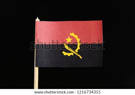 A official and national flag of Angola on toothpick on black background. Two horizontal bands of red and black with the Machete and gear emblem in the center.