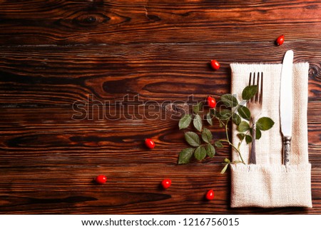 Thanksgiving table setting concept. Fork and knife with dog-rose leaves and berries on brown wooden table. November mood background with briar branches. Copy space, close up, top view, flat lay.
