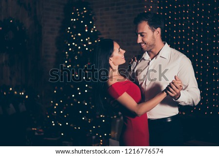 Profile side view photo of man in formal wear dance with attractive, cute, elegant, gorgeous lady in red dress in room with lights garland decorations on pine tree make big hollywood smile