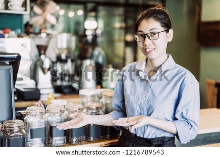 Cheerful barista showing coffee varieties and offering to buy tasty coffee. Positive young Asian restaurant manager presenting coffee. Drink establishment concept