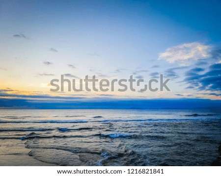 A photo of a gorgeous sunrise behind clouds and reflected over the waves of the Mediterranean Sea. It was taken on the Racó beach in Cullera, a touristic coastal town in Valencia, Spain, Europe