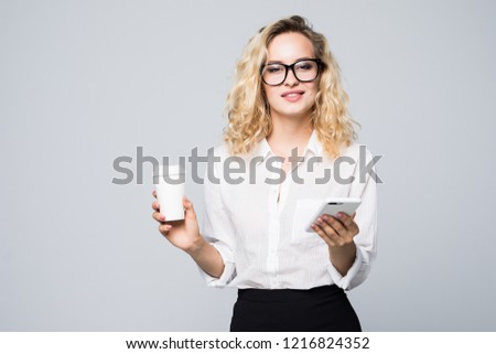 Portrait of a satisfied young business woman using mobile phone while holding cup of coffee to go isolated over white background