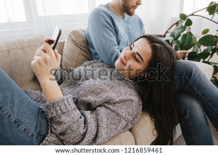 Couple obsessed with smartphones checking social networks at home using phone apps online, young man and woman texting or browsing on cellphones