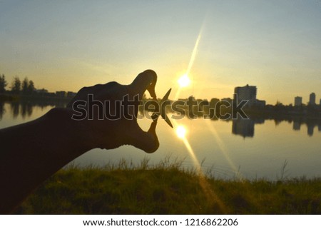 hand holding scissors picking on rising sun over water reflection