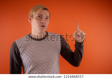 Handsome young man in grey sweater posing on orange background
