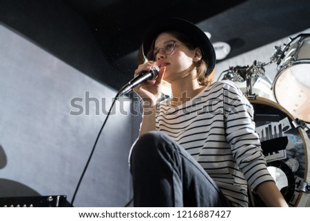 Low angle portrait of beautiful young woman singing to microphone during band rehearsal in studio, copy space