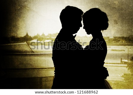 Silhouette of thai couple holding one another facing each other with background of thai temple. Picture was added with vignette and layered old style
