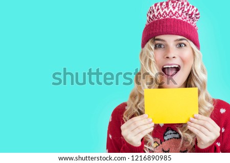 
very beautiful young girl of European appearance in a Christmas hat and a sweater with an advertising card in her hands
