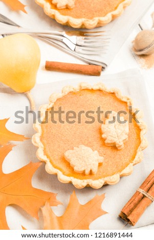 Pumpkin pie with cinnamon and cookies on gray napkins on white wooden background with autumn yellow leaves - top view close up photography of seasonal american traditional sweet baked food.