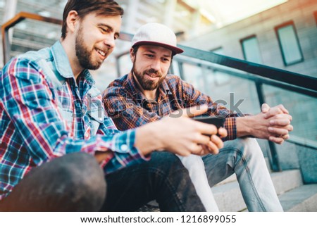 Virtual betting and real money winning concept. Two friends sitting on the stadium steps and using gambling mobile application ready to celebrate a victory.