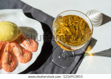 Wine in a glass on a background of seafood on a white dish in the shape of a shell in bright sunlight.