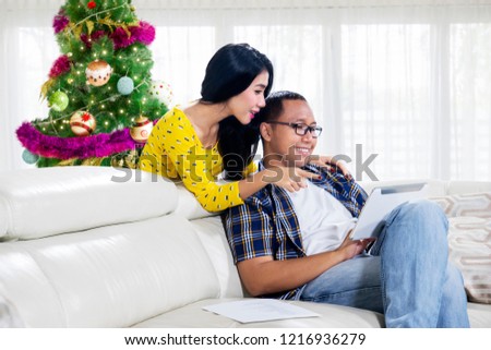 Picture of romantic couple using a digital tablet while sitting on the couch with Christmas tree at home
