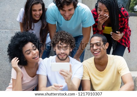 Group of international young adults gaming with phone outdoors in the city