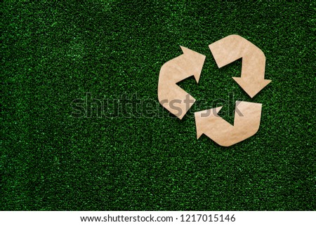 Eco recycle sign made of craft paper on green grass background top view space for text