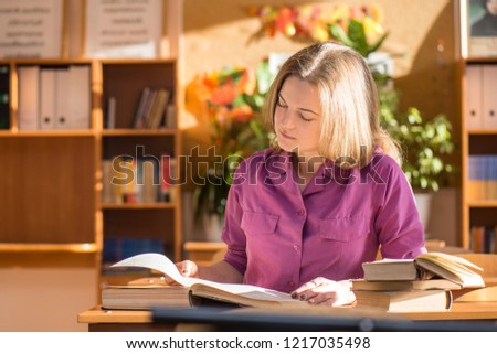 Girl student or teacher sits at her desk in the classroom, sunny day, and reads a book