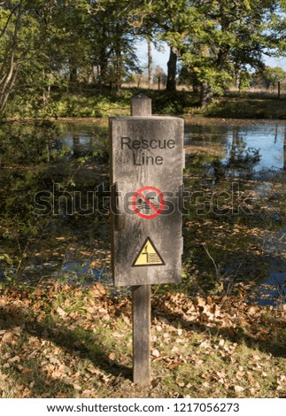 Wooden Box with a Rescue Line and Warning Signs for "No Swimming" and "Deep Water" by the Side of a Lake in Rural West Sussex, England, UK