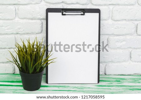 Office wooden clipboard standing against white brick wall, copy space