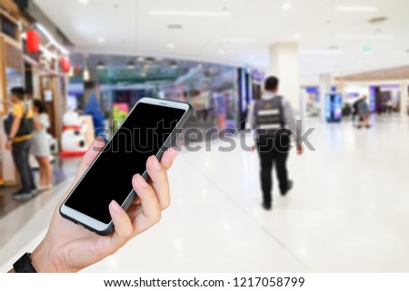 Man use mobile phone, blur image of the security guard in the mall as background.
