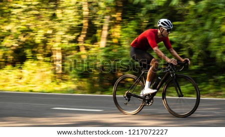 side view of Asian man in red cycling jersey on road bike. Speed, Competition, movement motion. Royalty-Free Stock Photo #1217072227
