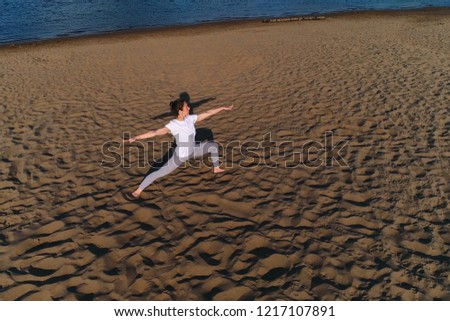 Woman doing yoga on the sand beach by the river in the city. Beautiful view.